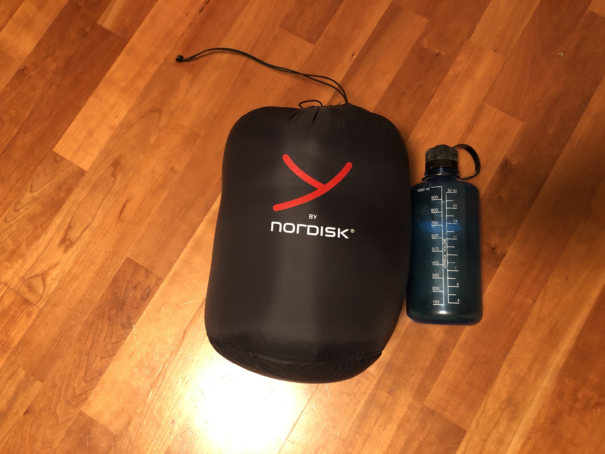 Schlafsack im Packsack mit Flasche daneben zum Größenvergleich