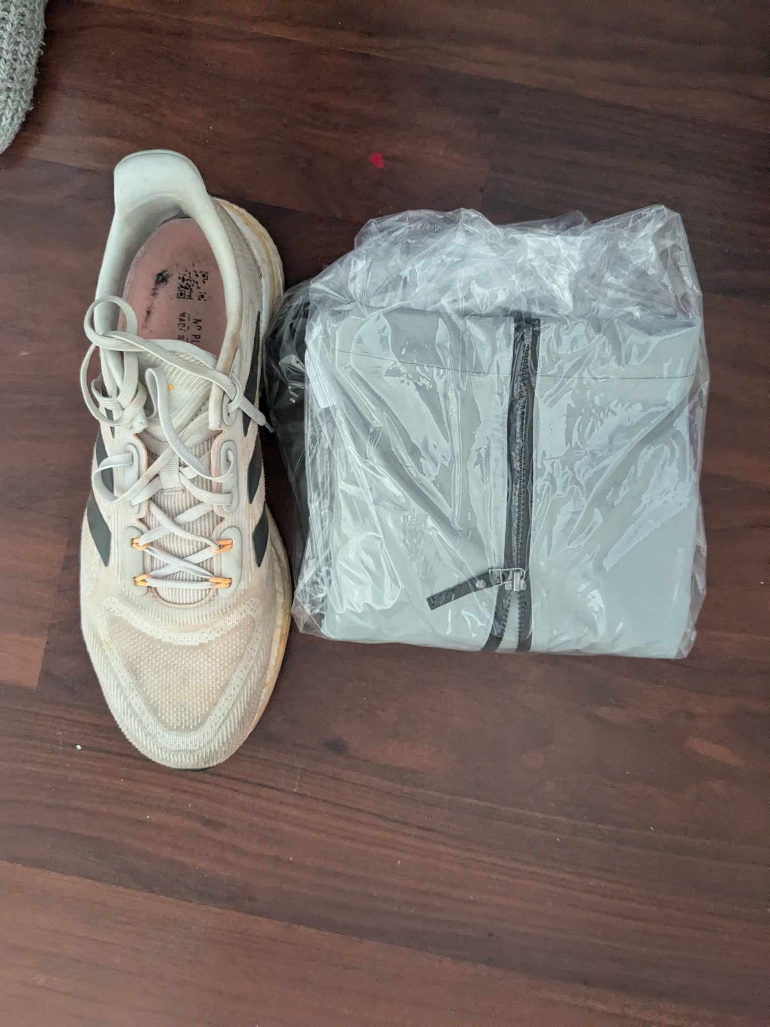 Man sieht die Jacke im Größenvergleich mit einem Schuh. Sie ist flacher und kurzer, dafür aber quadratisch gefaltet