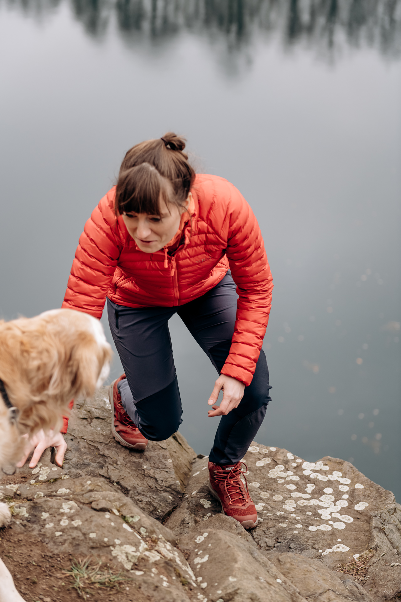 Frau steigt Felsen hoch, auf dem Hund wartet